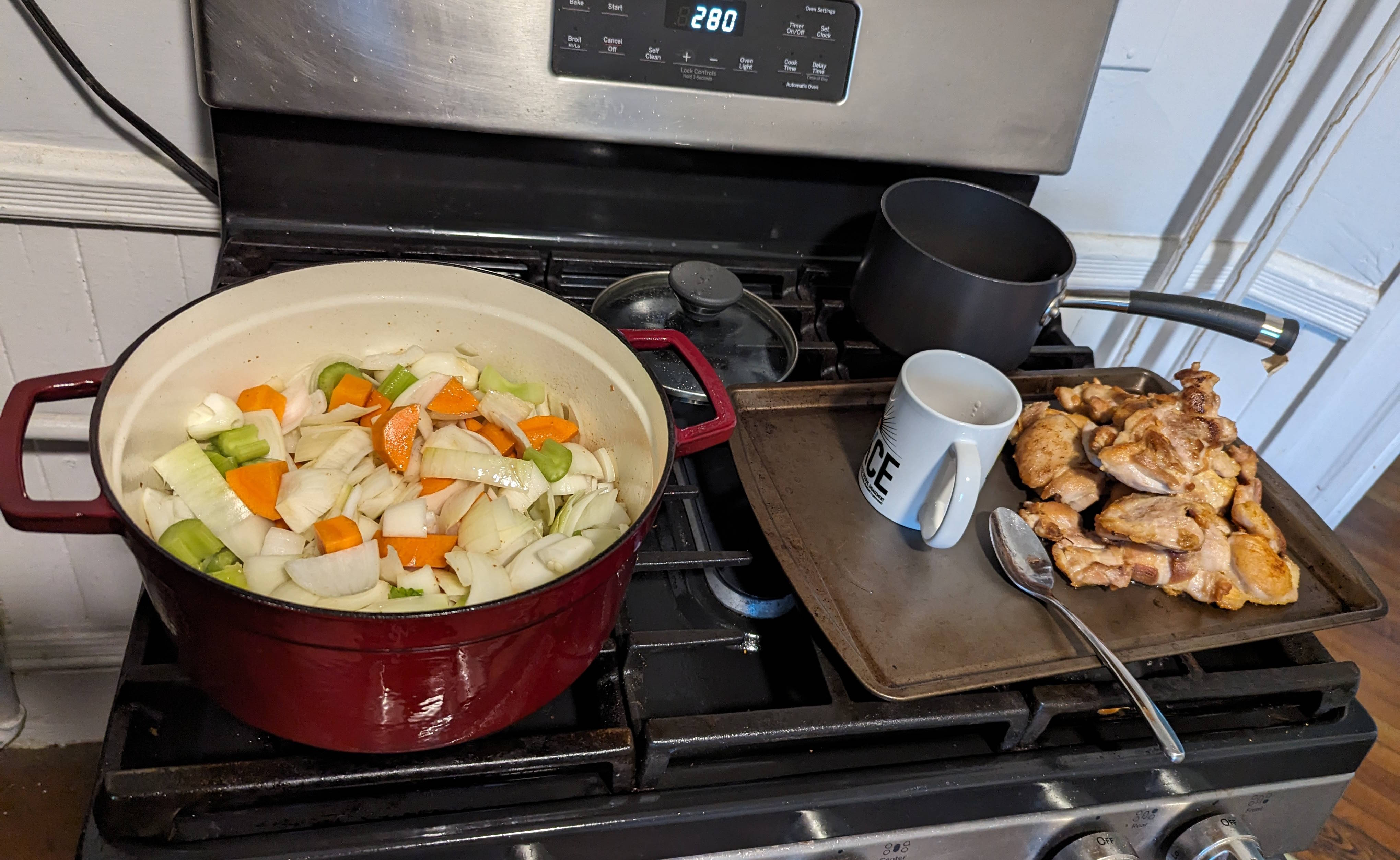 Dutch oven full of chopped onion, celery, carrot on the left, and a baking sheet with about two pounds of seared chicken on the right.