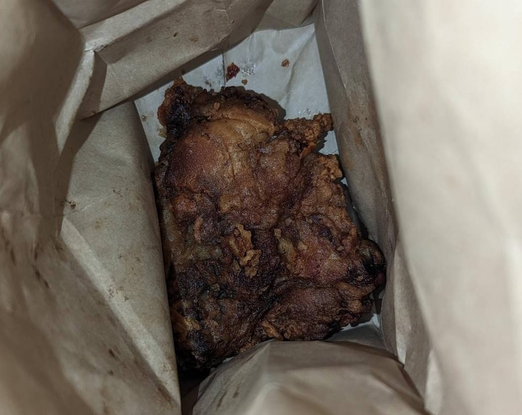 A close up of a fried chicken thigh in a paper bag.