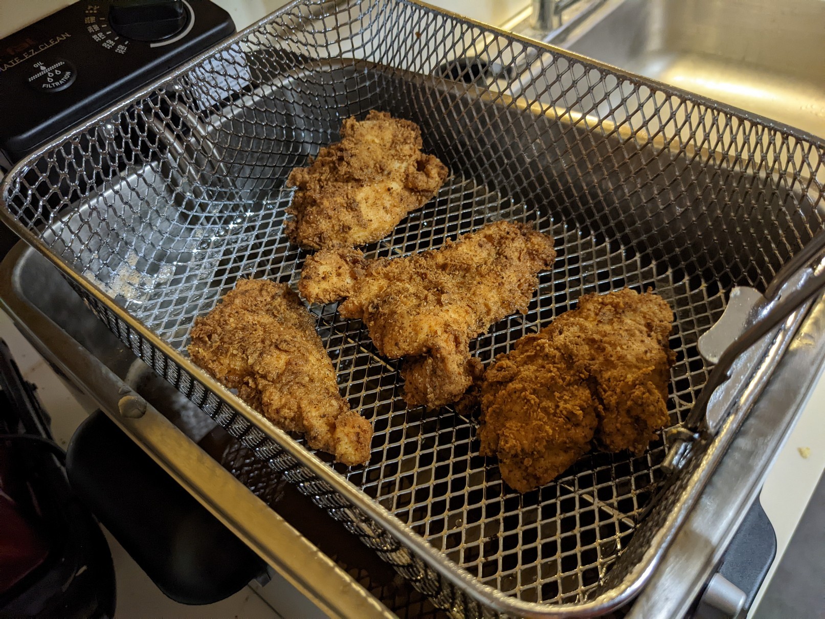 Pieces of fried chicken thighs in a fryer basket, draining from oil.