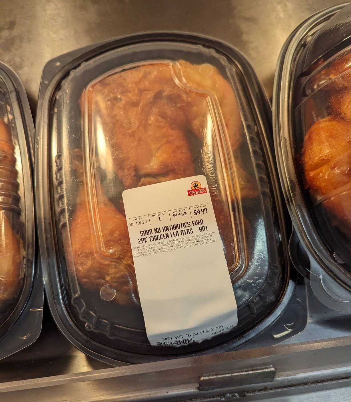 Roasted chicken quarters in plastic boxes on a heated foodservice shelf.